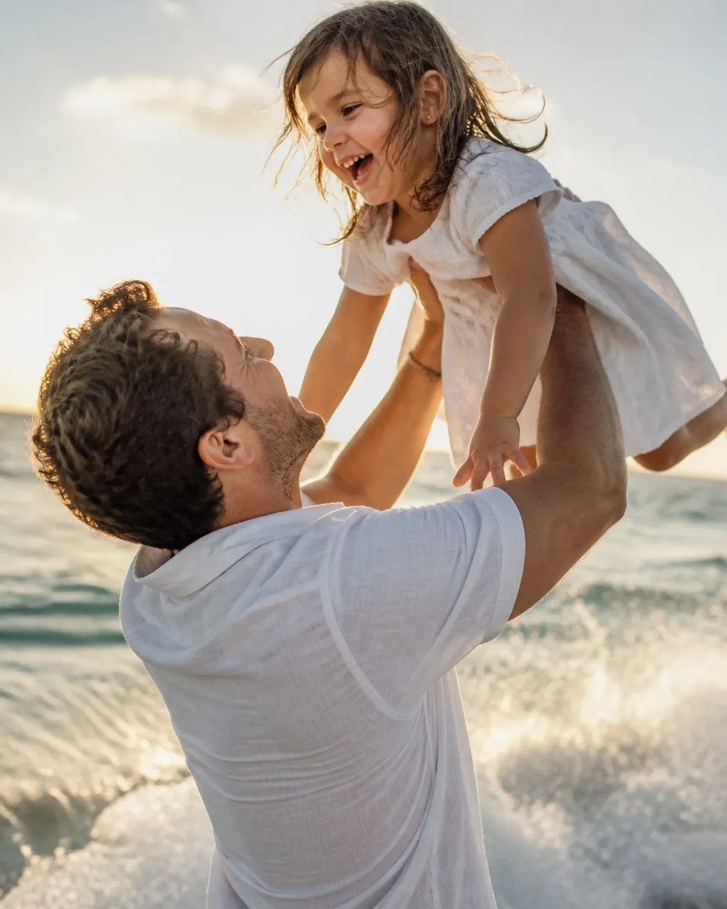 Parent lifting a laughing child near the Florida shoreline