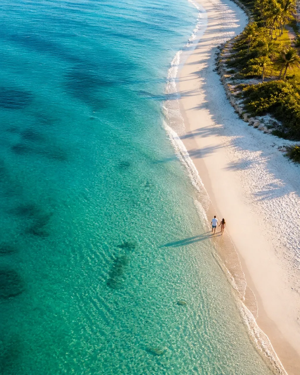 Aerial view of a couple walking along a turquoise Florida shoreline